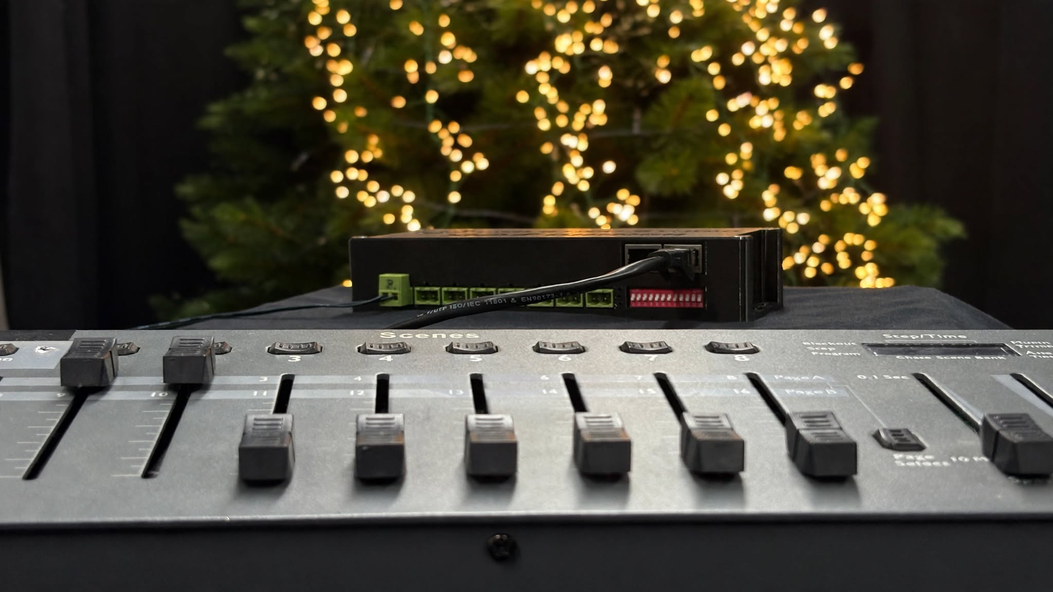 DMX lighting console with the Xmas Dimmer on top and a lit Christmas tree behind