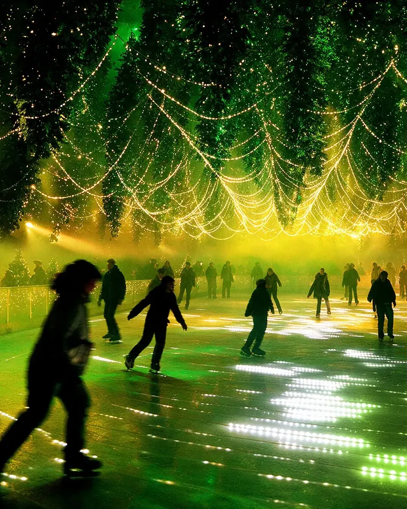 Skaters under hanging Christmas trees with string lights faded to green over DMX