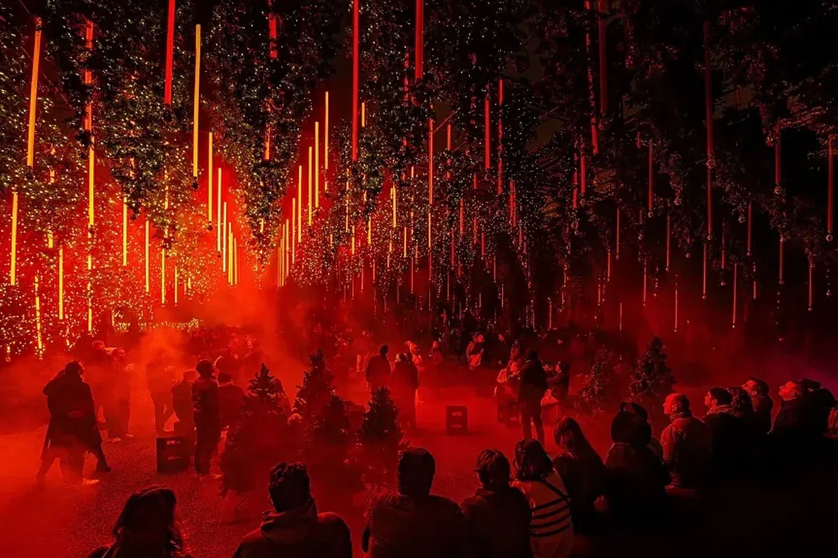 Visitors under hanging Christmas trees in red light and fog