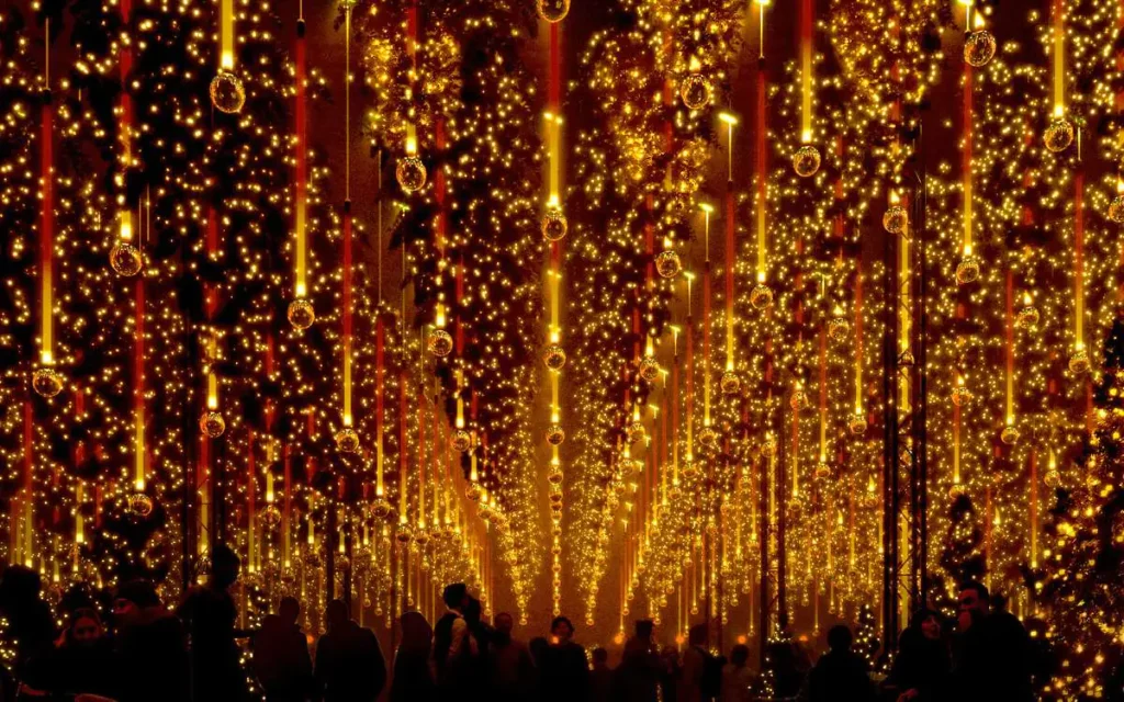 Warm gold Christmas light curtain with hanging icicle tubes and baubles above a crowd