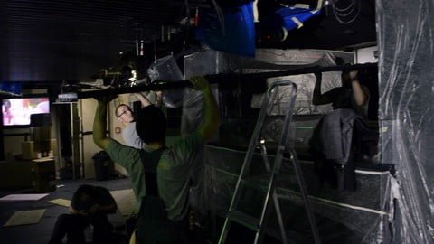 Three workers putting up a metal frame with LED strips and prepare it to be attached to ceiling.
